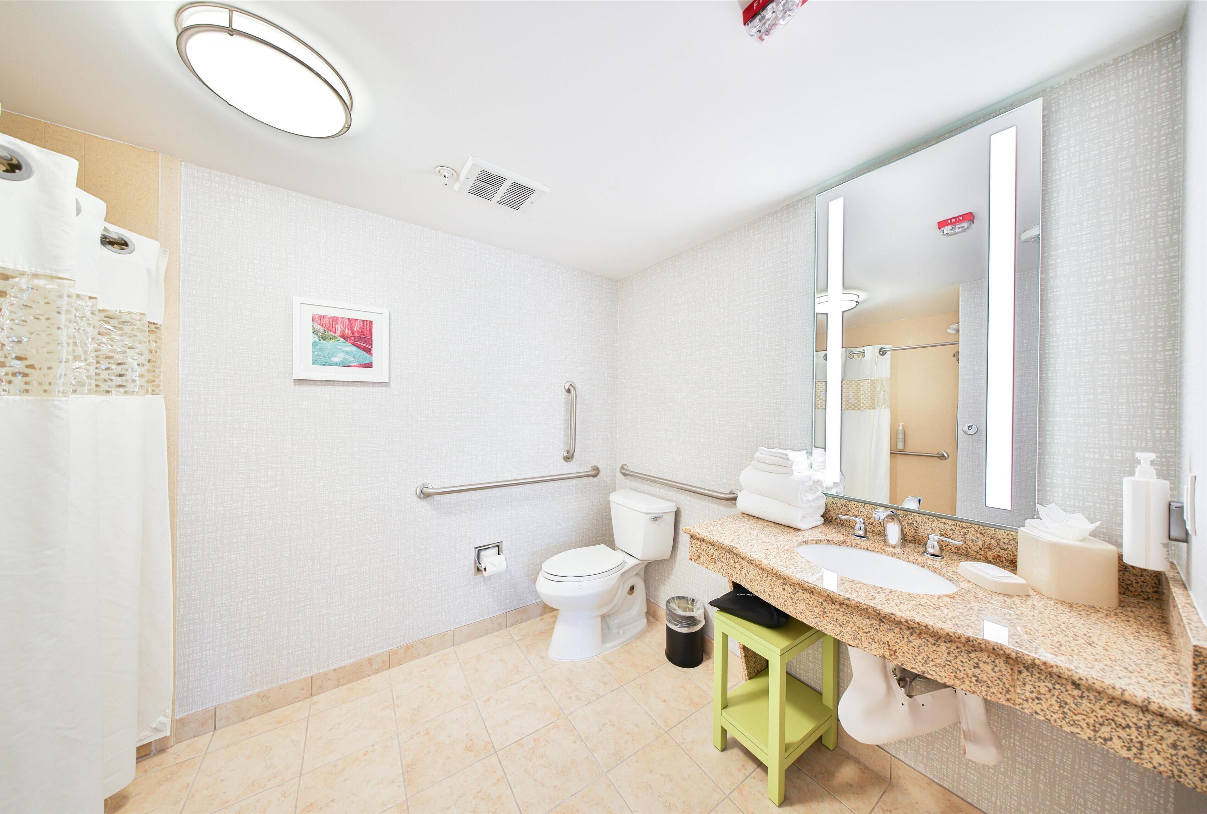 A modern bathroom with a large sink, toilet, and handrails.