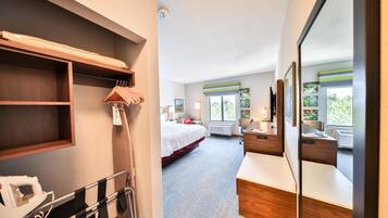 Quarto de hotel com cama, mesa de cabeceira, espelho e janela com vista para o verde.
