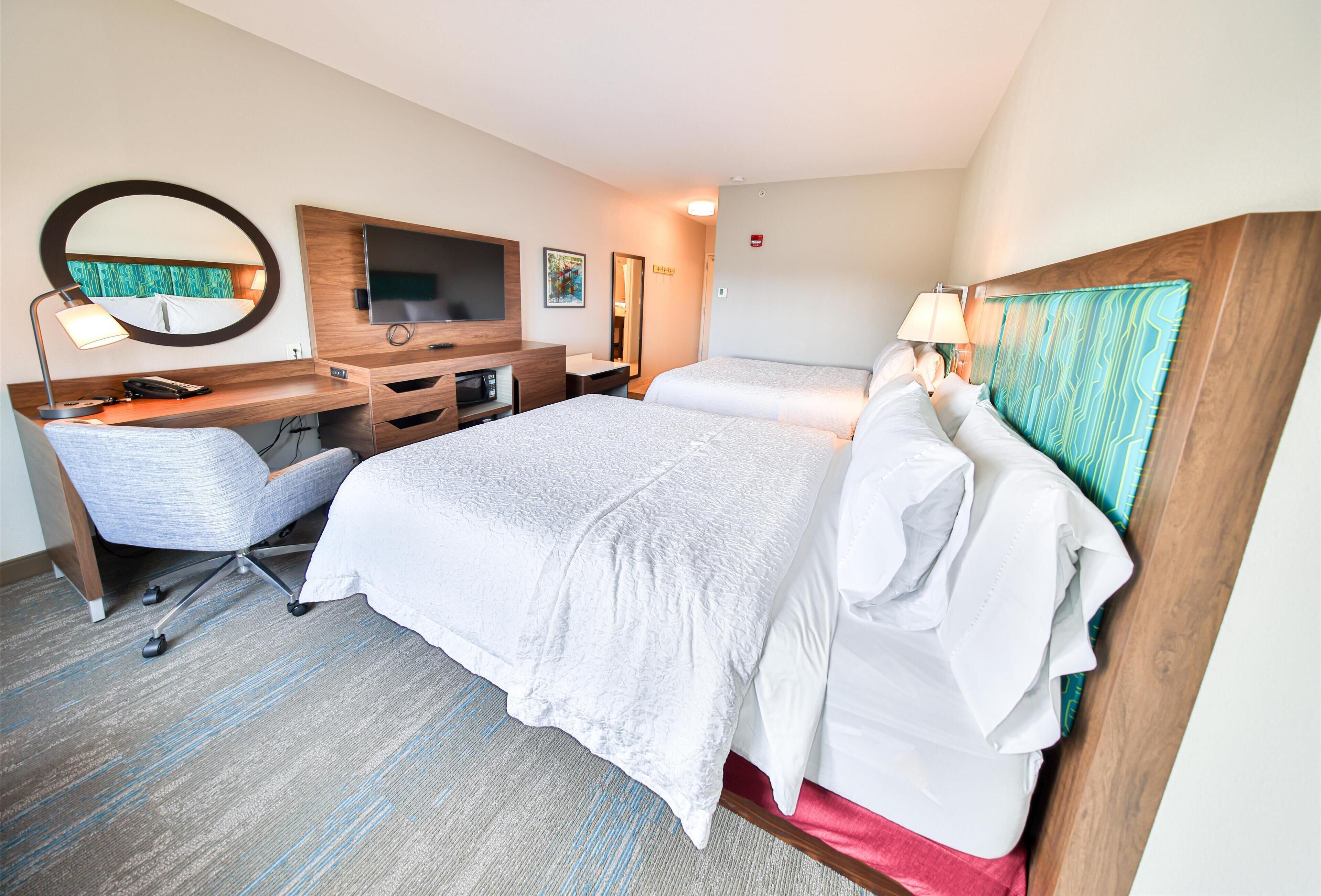 A hotel room with a bed, a desk with a chair, a TV, and a mirror.
