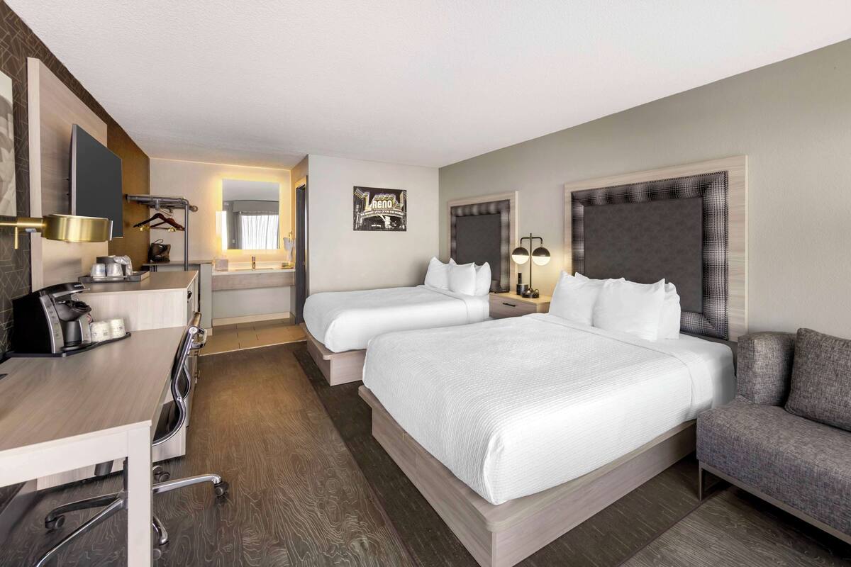 A hotel room with a large bed, a desk with a coffee maker, a chair, a sofa, and a mirror.