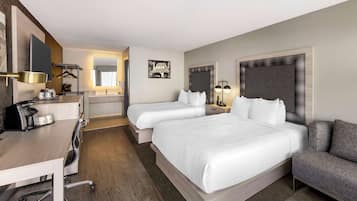A hotel room with a large bed, a desk with a coffee maker, a chair, a sofa, and a mirror.