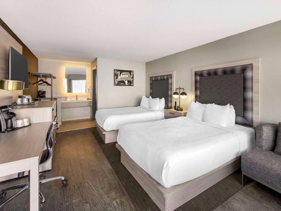 A hotel room with a large bed, a desk with a coffee maker, a chair, a sofa, and a mirror.