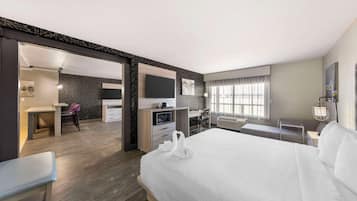 Una habitación de hotel moderna con una cama grande, un escritorio con una silla, un televisor y un área de descanso con vistas a la ciudad.