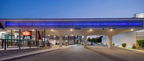 Entrada de um hotel com área de estacionamento coberta, placa indicando 'Aiden by BEST WESTERN' e design arquitetônico moderno com toldo iluminado em azul.