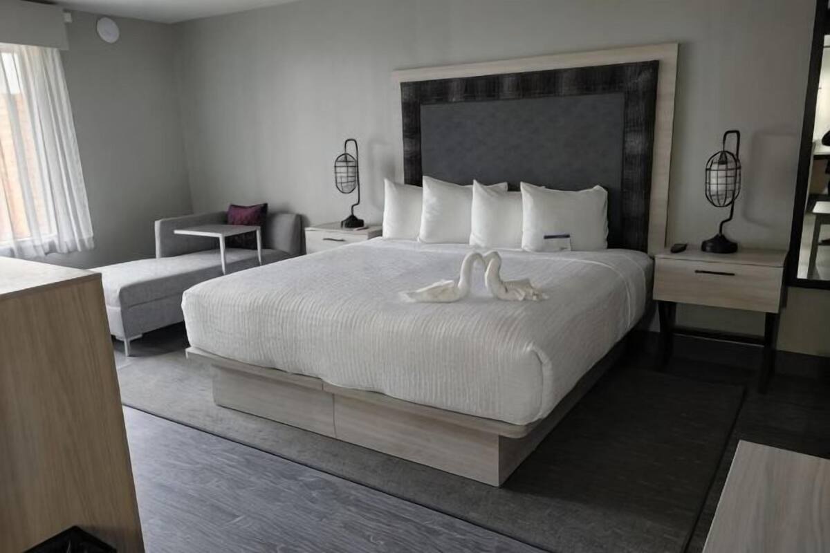 A modern hotel room with a large bed, bedside tables, a desk, and a chair.