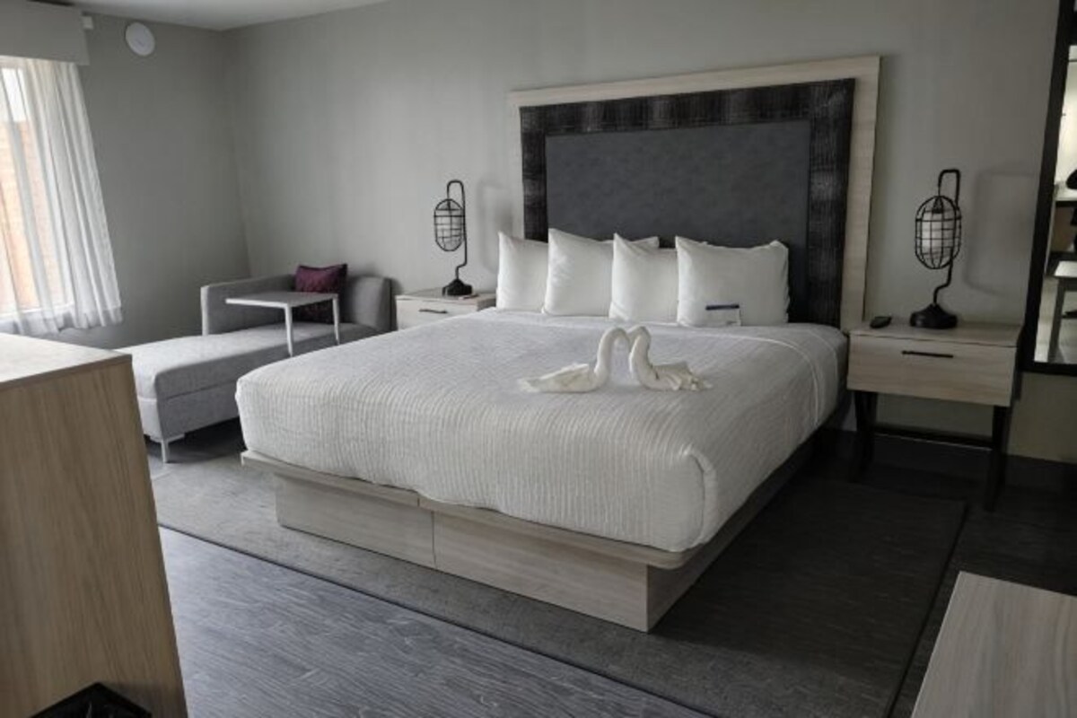 A modern hotel room with a large bed, bedside tables, a desk, and a chair.