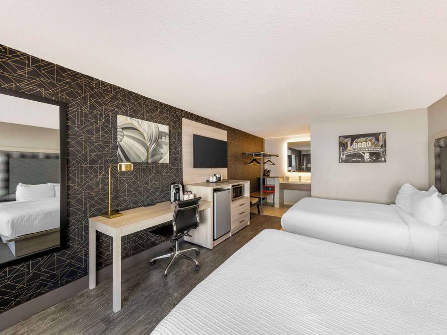 A hotel room with a large bed, a desk with a chair, a small kitchenette, and a mirror.