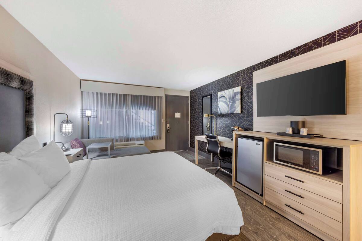 A hotel room with a large bed, a desk with a computer, a microwave, and a TV.