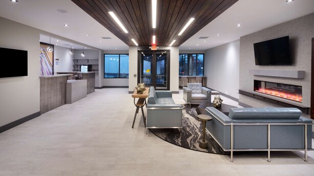 A modern living area with a sofa, a coffee table, and a fireplace. There is a kitchen area with a refrigerator and a television mounted on the wall. - Aiden by Best Western South Reno (Reno)