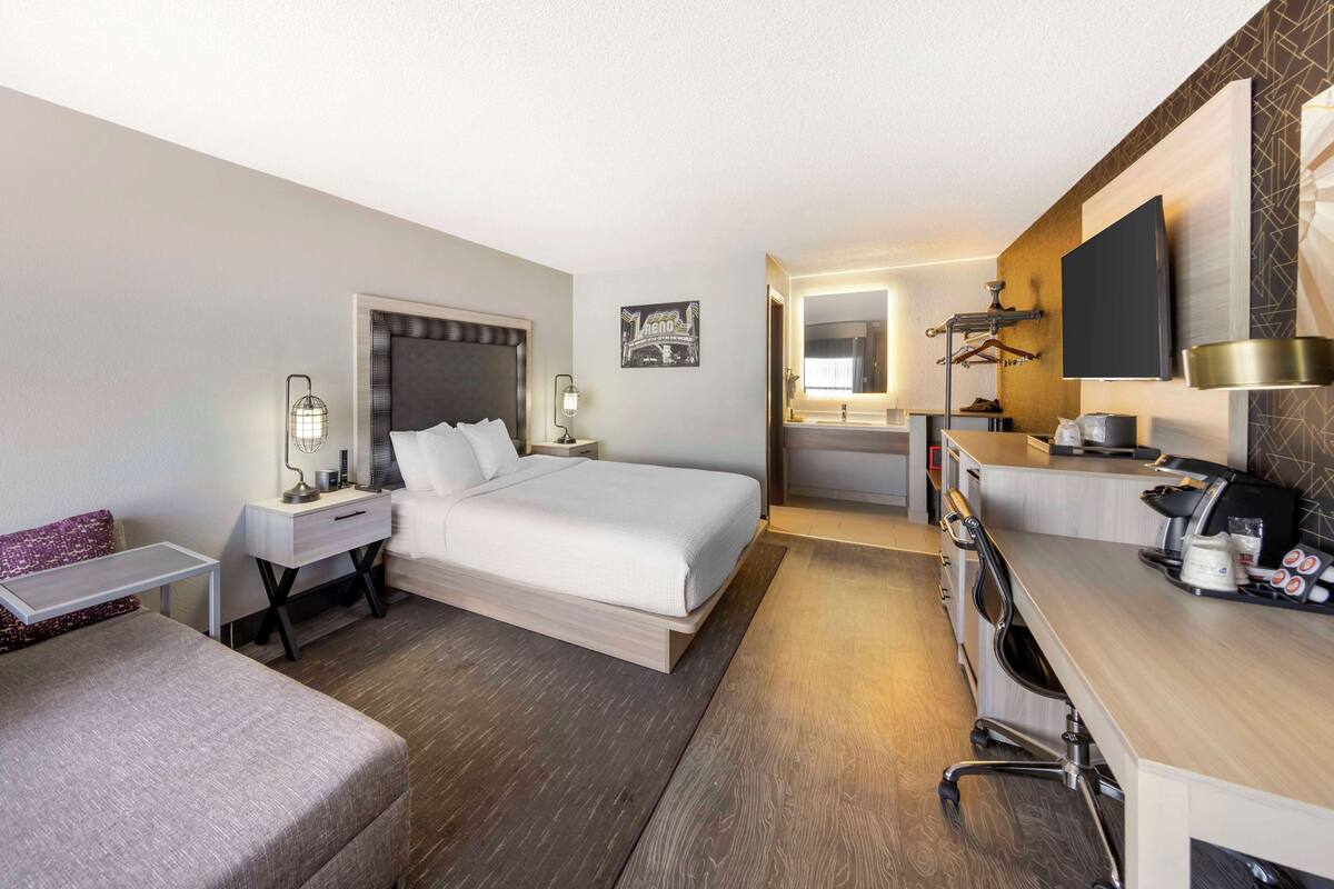 A hotel room with a bed, bedside table, lamp, desk, chair, and a TV.