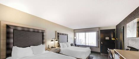 A hotel room with two beds, a desk, a chair, a dresser, and a large window with curtains.
