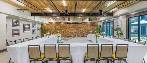 Un salón de conferencias con una larga mesa, sillas y una pared de ladrillo.