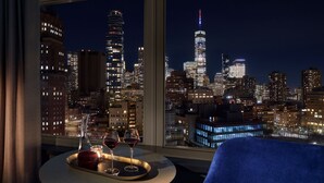 Vista panorámica de la ciudad desde una ventana, con una bandeja de copas de vino y un cuenco rojo sobre una mesa redonda.