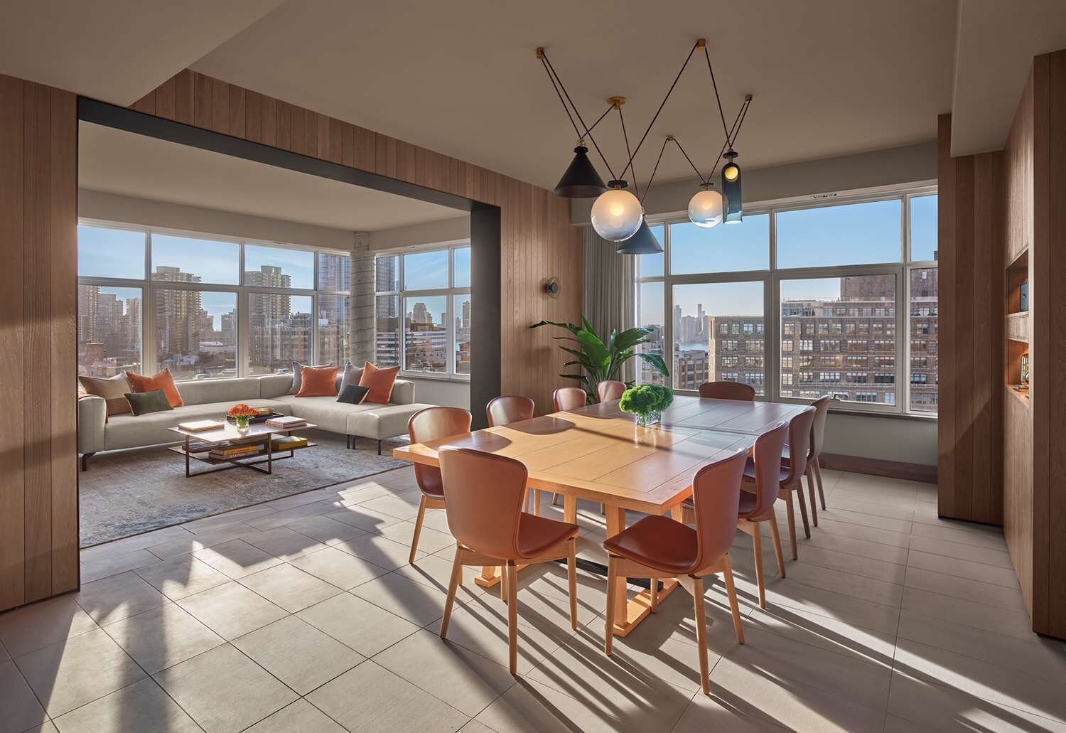 A spacious living area with a large dining table, comfortable seating, and a city view through large windows.