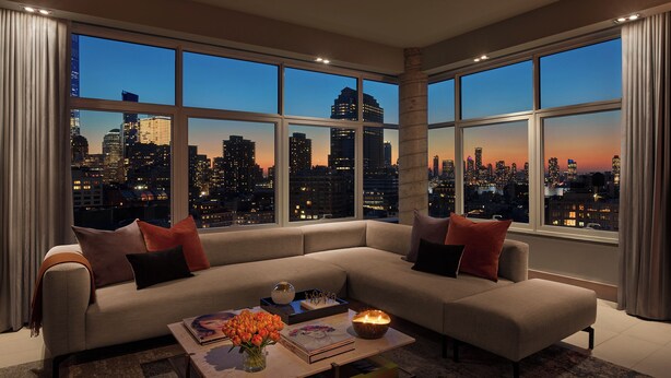 Una sala de estar moderna con un sofá seccional grande, una mesa de centro con libros y flores, y vistas a la ciudad a través de amplias ventanas.