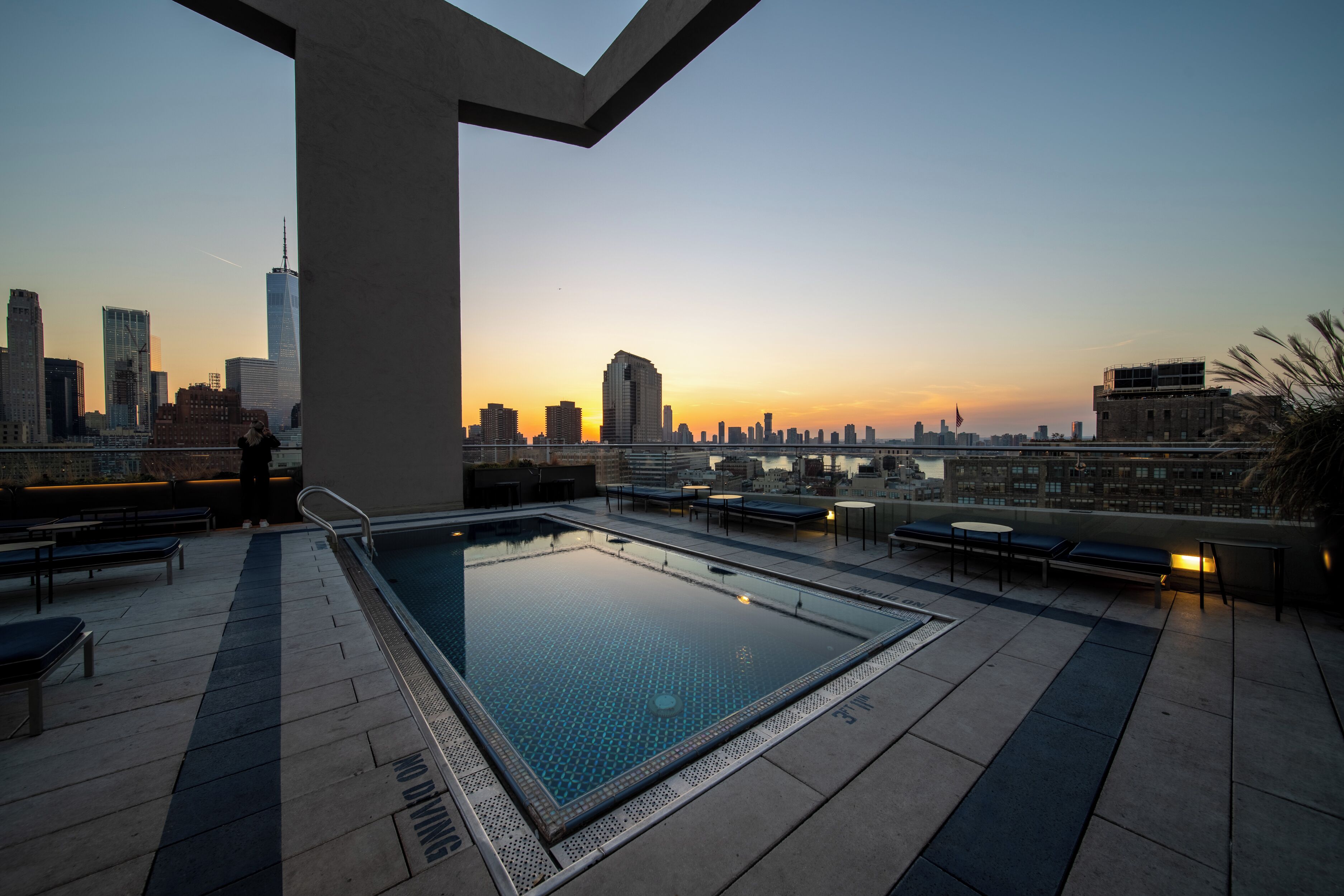 An outdoor infinity pool with a city skyline view at sunset.