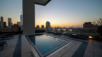 An outdoor infinity pool with a city skyline view at sunset.