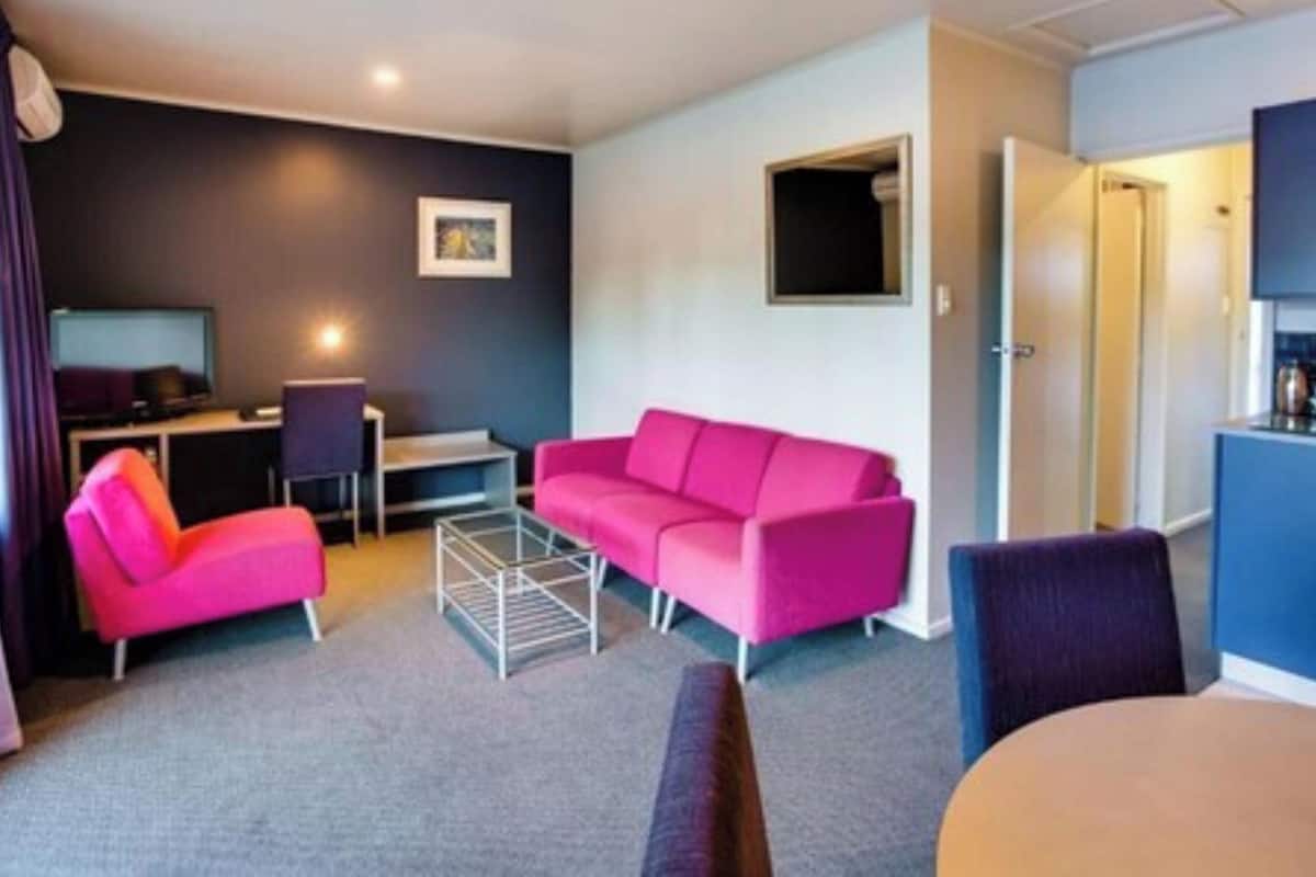 Una habitación de hotel moderna con un sofá rosa, un escritorio pequeño, una silla y una mesa de comedor.