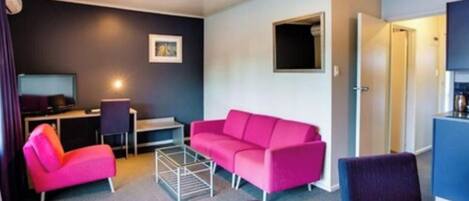 Ein modernes Hotelzimmer mit einem rosafarbenen Sofa, einem kleinen Schreibtisch, einem Stuhl und einem Esstisch.