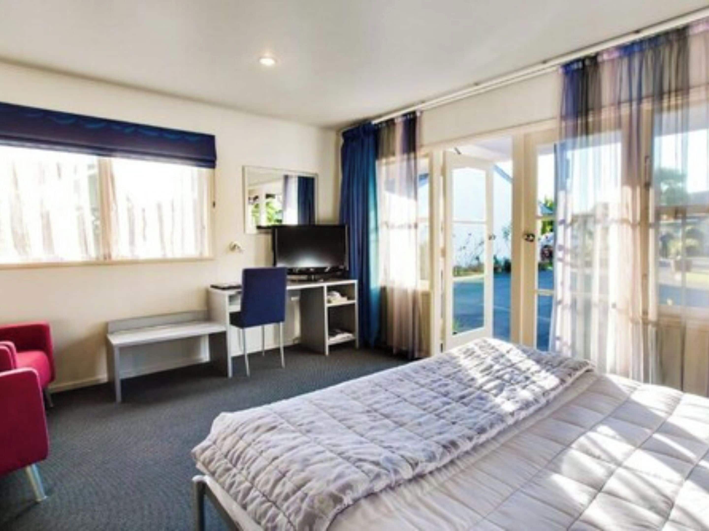 Une chambre d’hôtel avec un lit, un bureau, une chaise et un téléviseur.