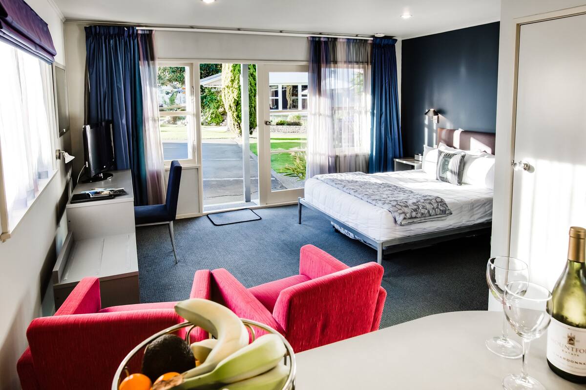 Una habitación de hotel con cama, escritorio, silla, mesa de comedor y una botella de vino.