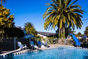 Ein Swimmingpool mit blauer Rutsche, Liegestühlen und Palmen.