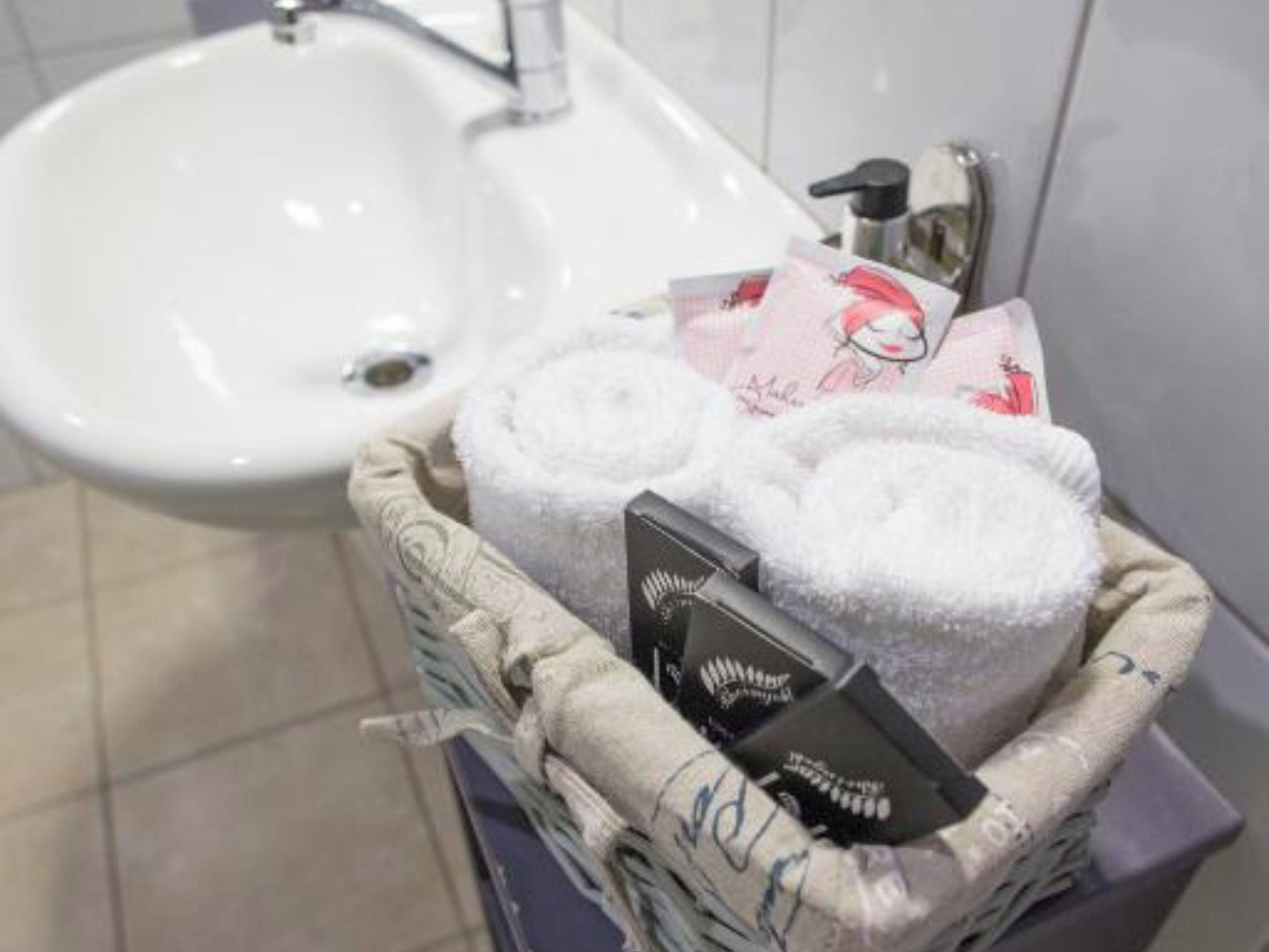 Et badeværelse med en hvid vask og en kurv med håndklæder og toiletartikler.