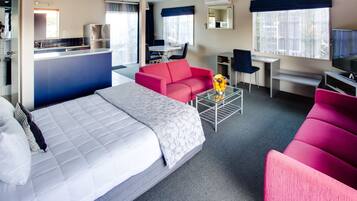 Een hotelkamer met een bed, een rode bank, een bureau met stoel, een televisie en een keukenhoek.