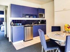 Una cocina moderna con armarios azules, un lavavajillas de acero inoxidable y un microondas. Hay una zona de comedor con una mesa redonda y dos sillas.
