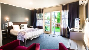 Habitación de hotel con una cama, dos sillas rojas, un escritorio con una computadora y un ventanal corredizo al exterior.