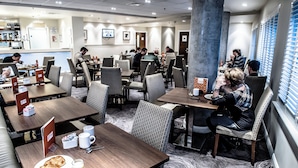Ein Essbereich eines Hotels mit mehreren Tischen und Stühlen, einer Kaffeestation und einem Fernsehbildschirm.