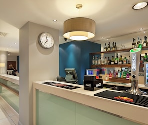 A hotel reception area with a clock, a bar counter, and a variety of liquor bottles. - Holiday Inn Express Manchester CC - Oxford Road by IHG (Manchester)