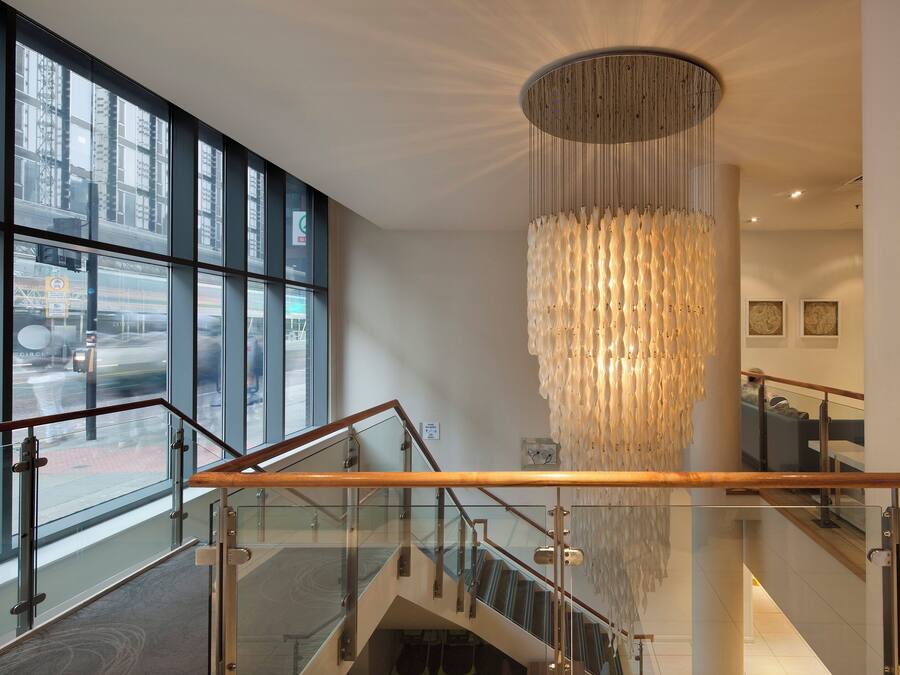 Een moderne hotellobby met een glazen trap, een grote kroonluchter en uitzicht op de straat door middel van ramen van de vloer tot aan het plafond.