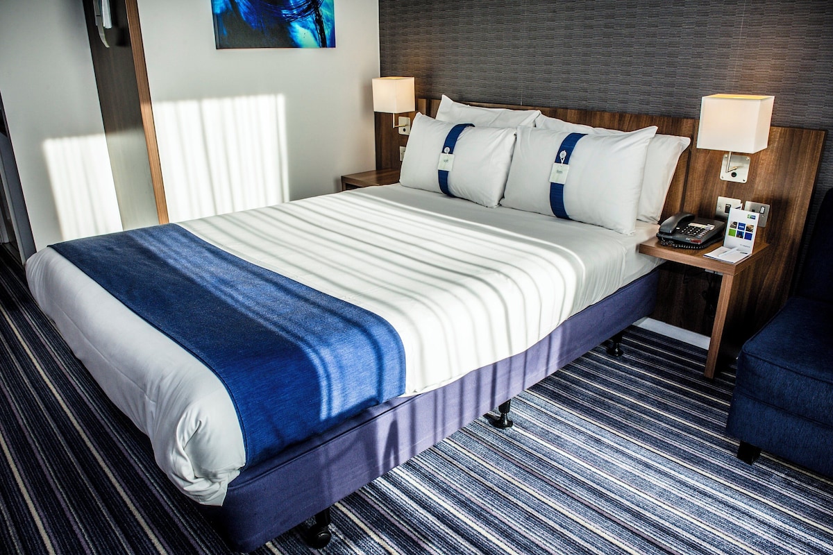 Quarto de hotel com cama, mesas de cabeceira, abajur e telefone.