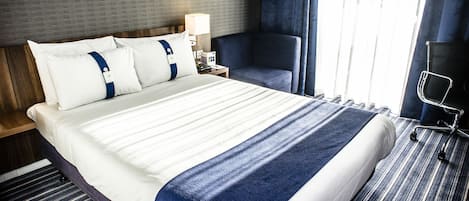 A hotel room with a large bed, a bedside table with a lamp, a chair, and a TV.