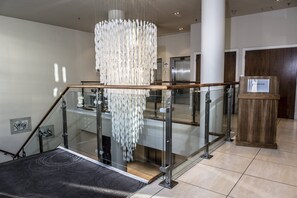 A modern hotel lobby with a glass staircase, a chandelier, and a reception desk.