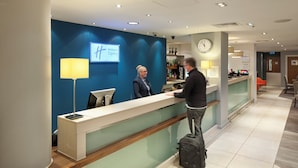 Ein Hotel-Rezeptionstresen mit einem digitalen Bildschirm, der 'Holiday Inn Express' anzeigt, und einer Wanduhr.