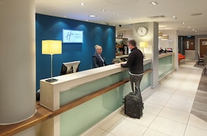 A hotel reception desk with a digital screen displaying 'Holiday Inn Express' and a clock on the wall. - Holiday Inn Express Manchester CC - Oxford Road by IHG (Manchester)