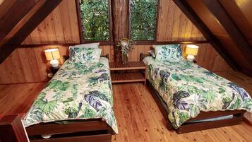 A room with two wooden beds, each with a floral bedspread and two pillows. There are two wall-mounted lamps on either side of the beds.