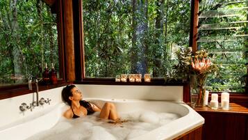 A woman relaxing in a bathtub with a view of lush greenery outside.