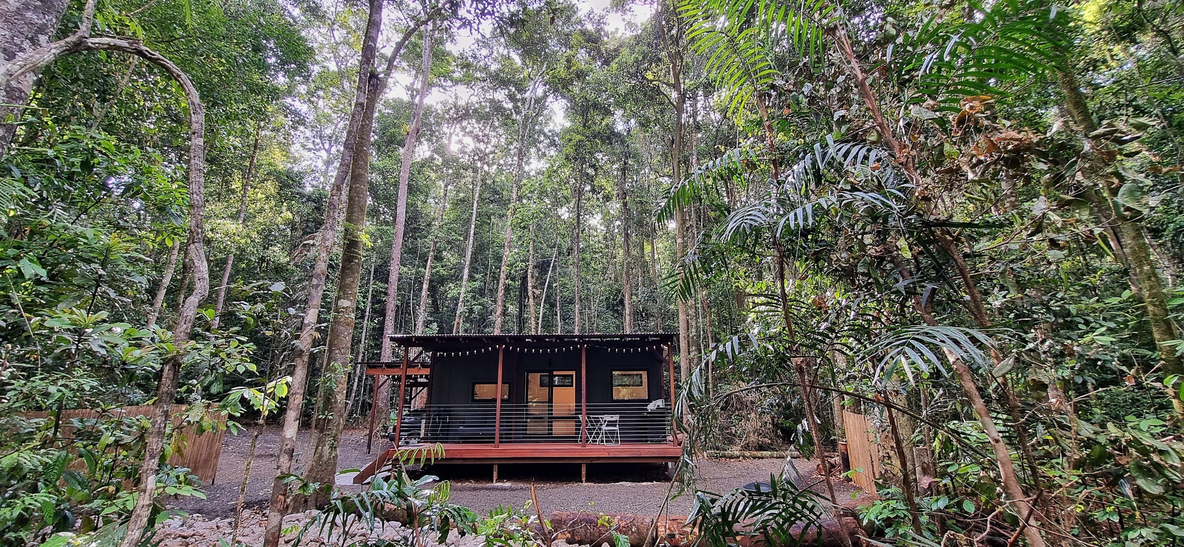 Uma cabana rodeada por uma floresta densa, com varanda e um pequeno alpendre.