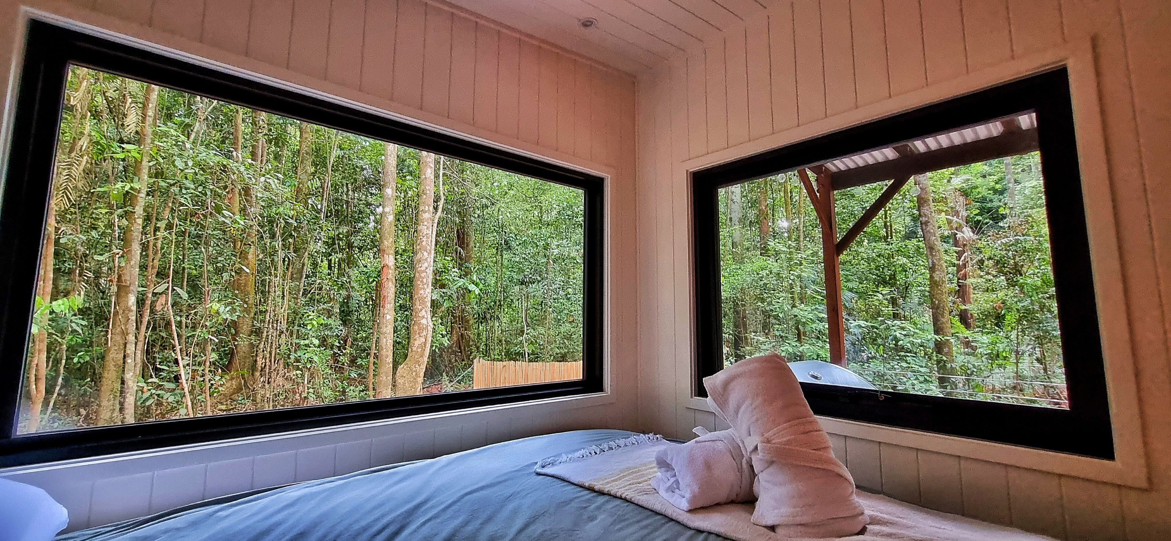 Une chambre avec deux grandes fenêtres, un lit et une vue sur une forêt.