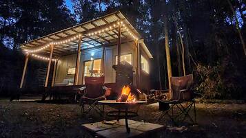 Una cabana amb un porxo cobert, una zona de foc i vista al bosc.