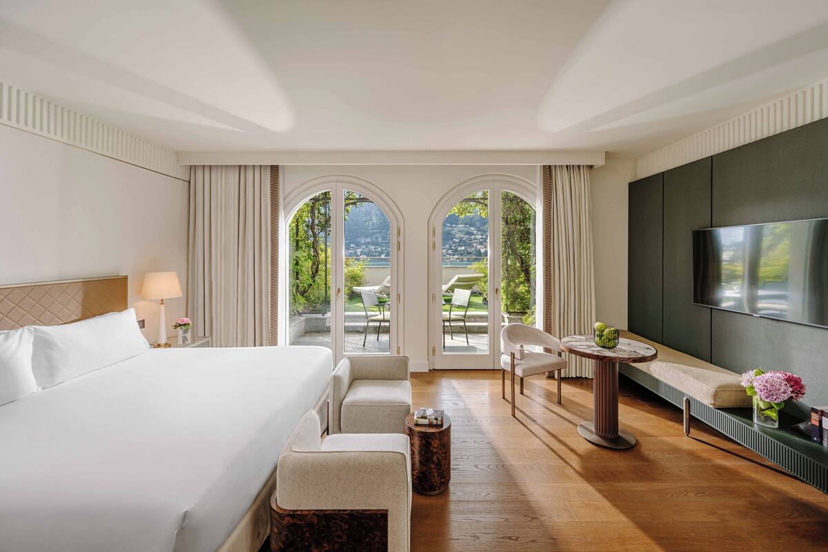 A hotel room with a large bed, a TV, a seating area with a table, and a view of the outdoors.
