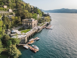 Una propiedad junto al lago con un muelle, barcos y un edificio grande con terraza con vistas al agua.