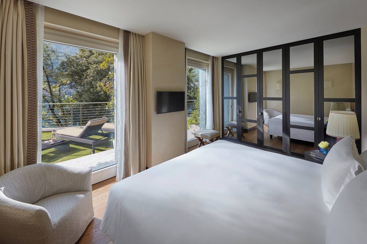A hotel room with a large bed, a sofa, a TV, and a balcony with a pool.