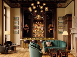 A bar area with a chandelier, bar stools, and a green sofa.