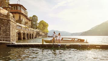 Un bâtiment historique en pierre, doté d’une jetée qui s’avance dans un lac, et entouré d’arbres et de montagnes.