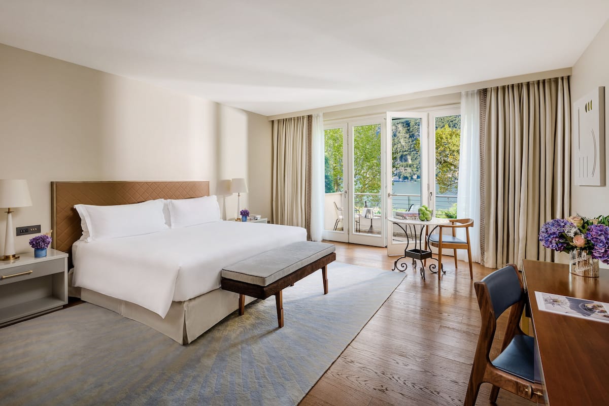Habitación de hotel con una cama grande, una mesita, una silla, un banco y vistas al exterior.