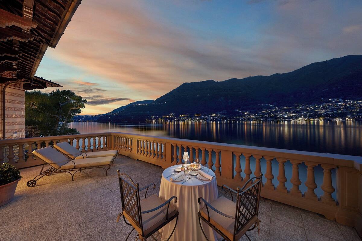 A terrace with a table set for dining, overlooking a lake and mountains at dusk.